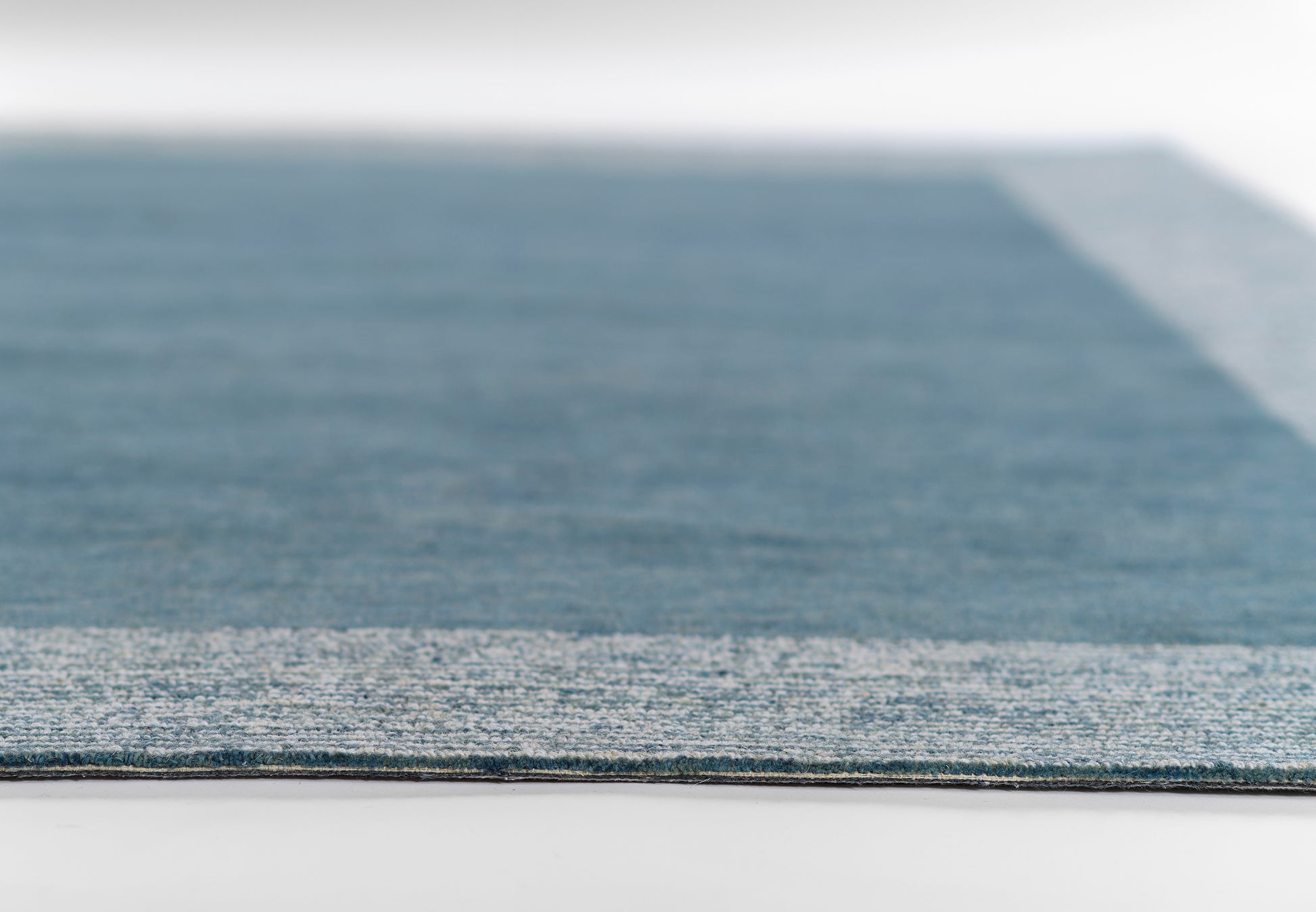 Blue rectangular flat-weave runner rug close-up with darker field and light border, textured fabric edge.