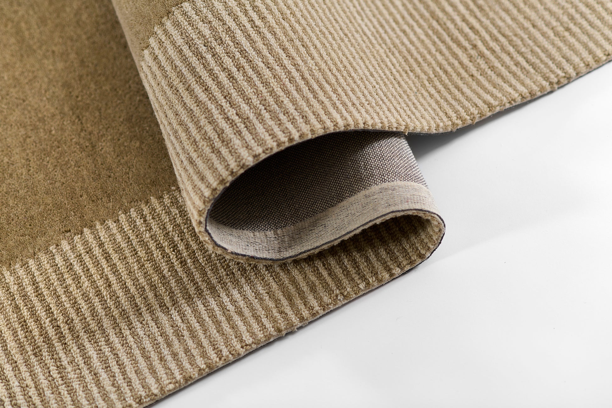 Beige wool rug with tan striped border, folded to reveal soft pile and underside.