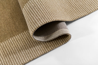Beige taupe woven rug with ribbed texture and striped border, folded corner showing underside.