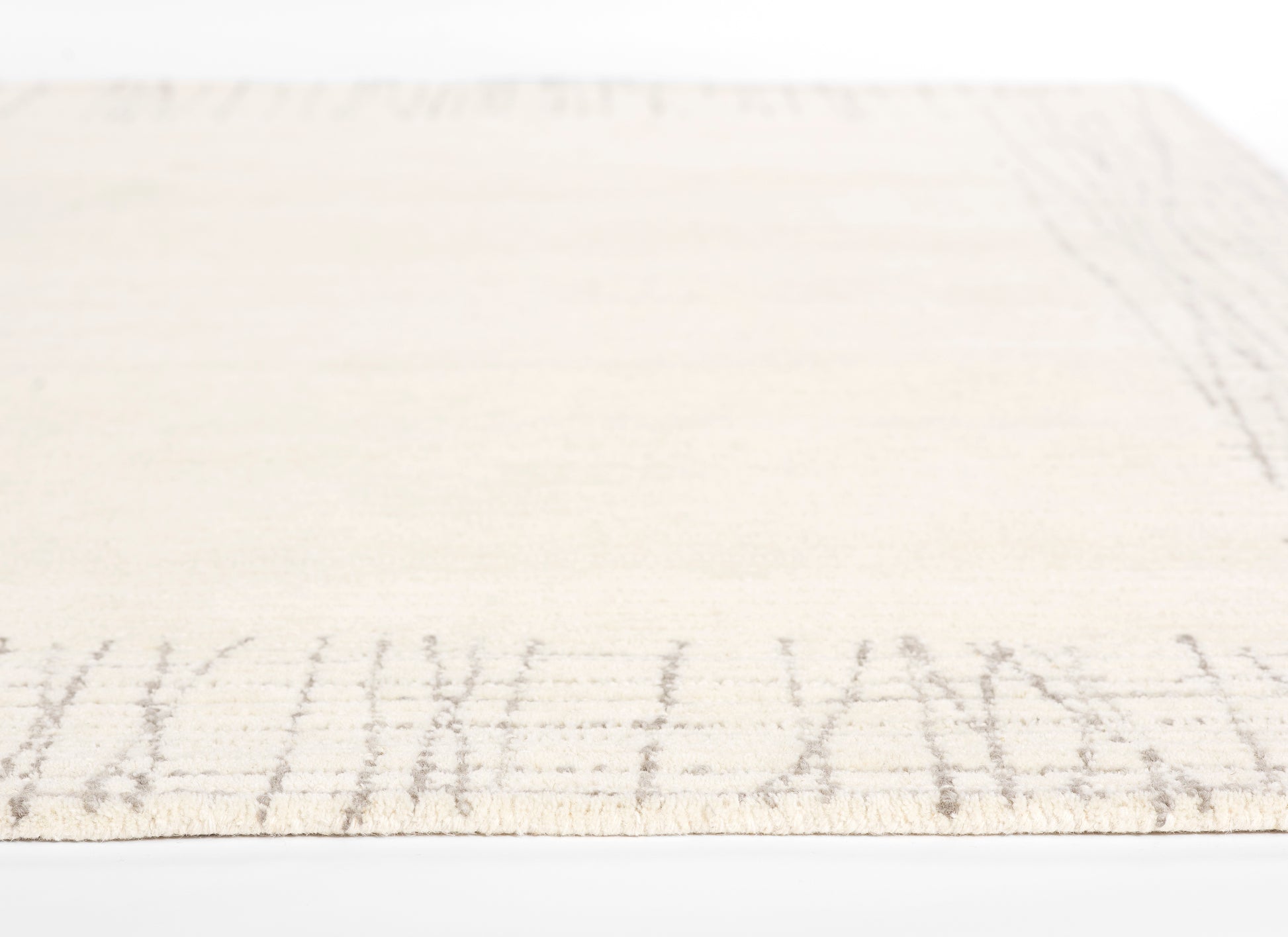 Rectangular cream flat-weave rug with a light taupe border motif; soft, neutral home decor.