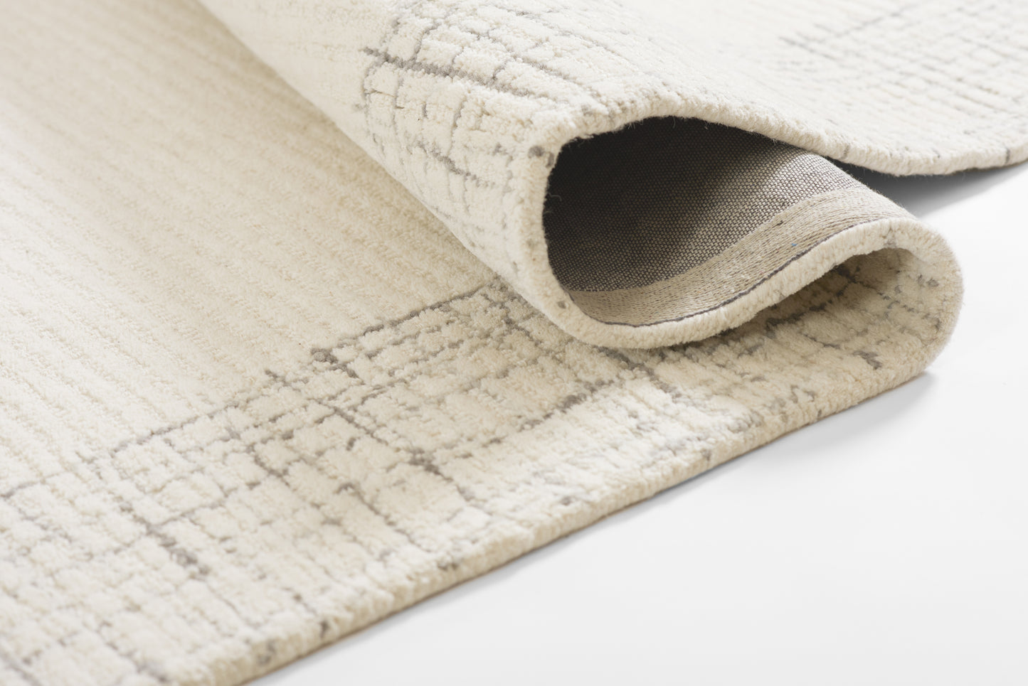 Cream woven rug with a subtle grid pattern, rolled edge showing soft underside and texture.