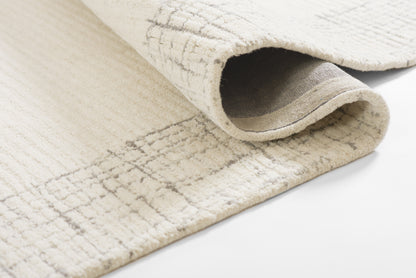Cream woven rug with a subtle grid pattern, rolled edge showing soft underside and texture.