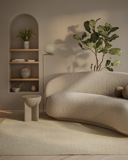 Curved ivory boucle sofa in a cozy living room with beige rug, wooden alcove shelves, and a large leafy ivy plant.