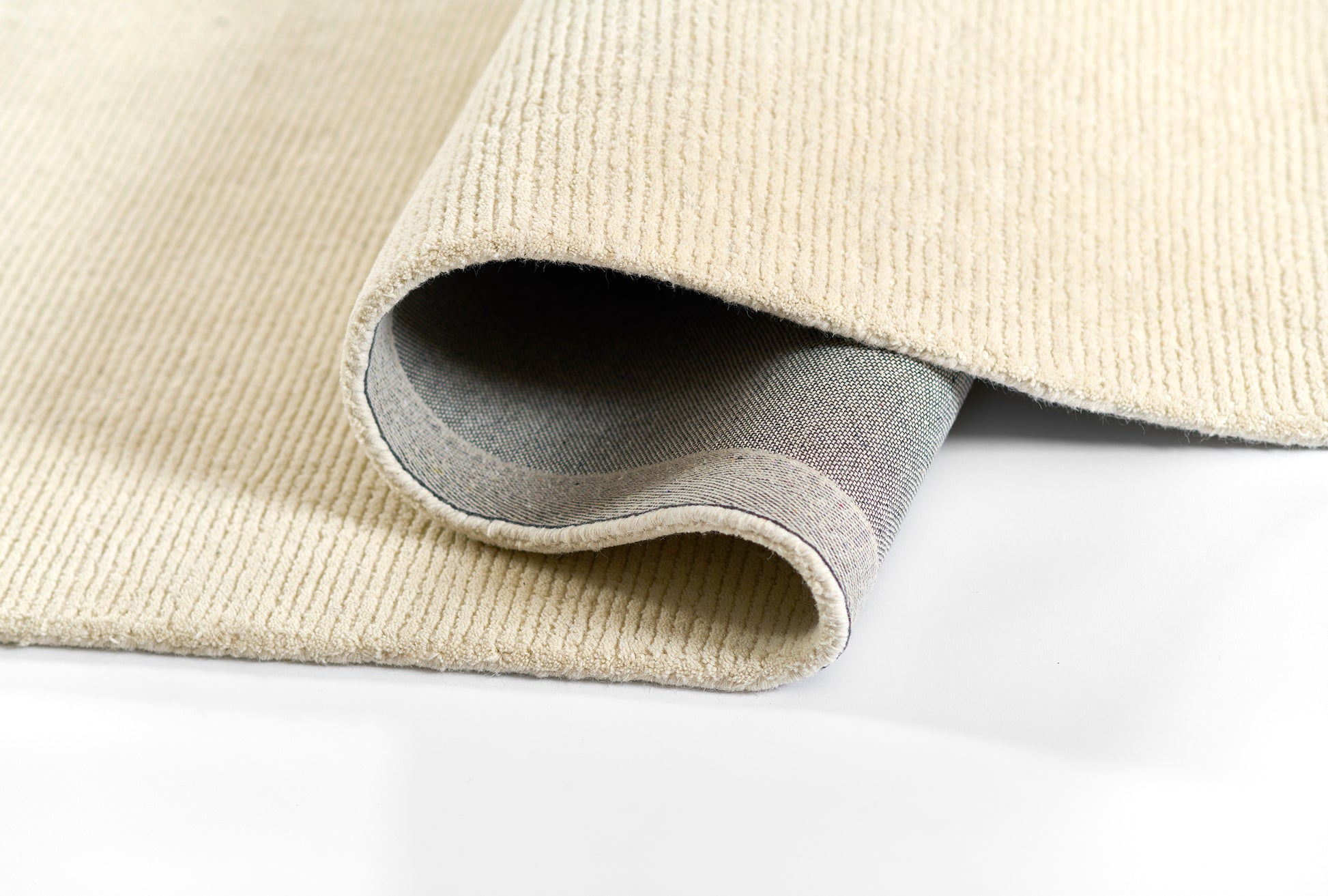 Beige ribbed woven rug partially rolled to reveal gray underside, cozy home decor accent.
