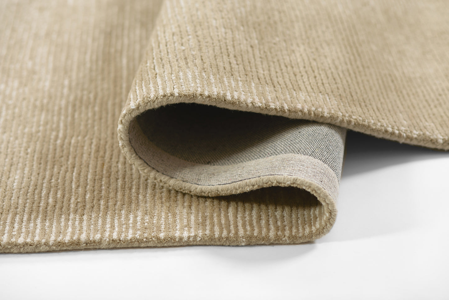 Beige ribbed rug with light vertical stripes, soft pile, rolled edge showing texture; ideal for living room or entry.