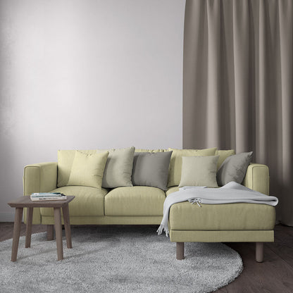 Light lemon-white solid fabric sectional with chaise, muted cushions, wooden legs, and a gray throw in a modern living room.