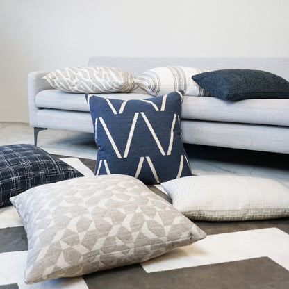 Navy blue chevron pillow with white zigzags among gray and cream geometric cushions on a light gray sofa.