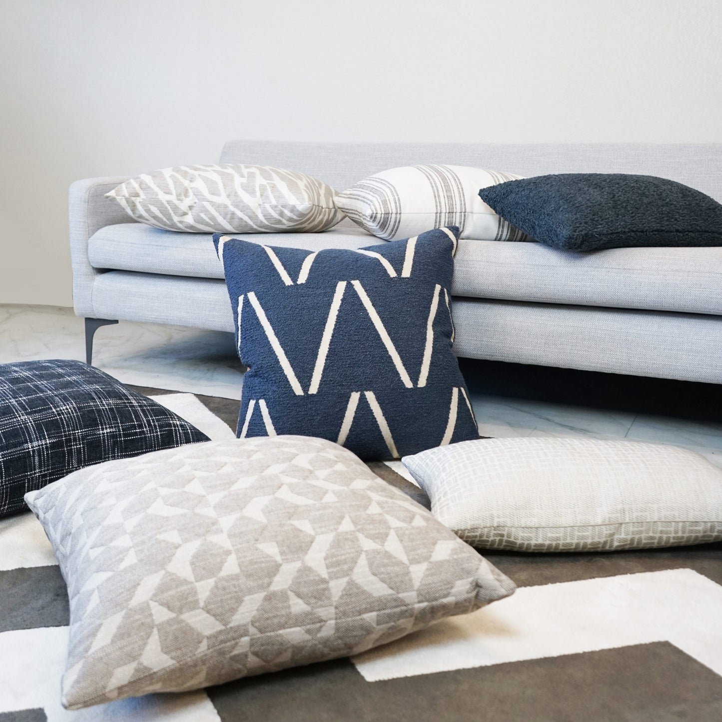 Blue domino plaid check throw pillow on a light gray sofa, surrounded by beige, cream, and dark blue cushions.
