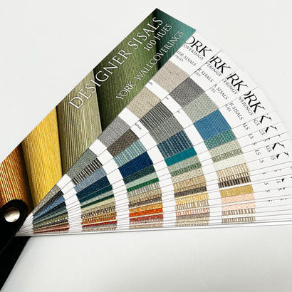 Color swatch fan deck of grasscloth wallpaper samples in a curved arrangement, showing woven textures in brown tones.