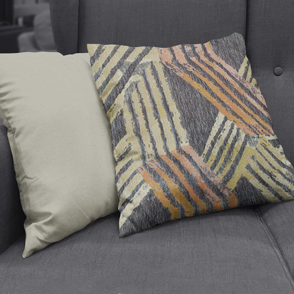 Beige solid pillow beside a gray abstract striped cushion with cream, gray, yellow & orange lines on a dark sofa.