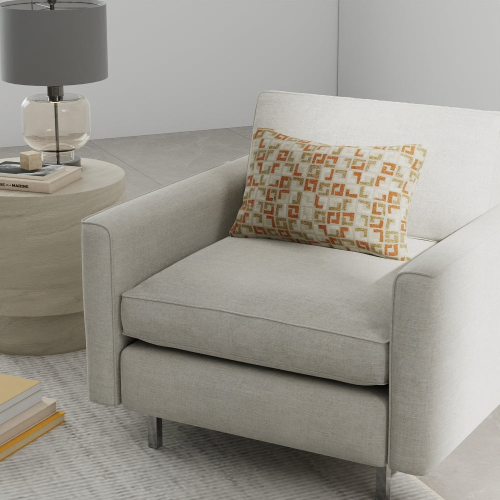 Light gray fabric armchair with matching ottoman and an orange geometric-patterned cushion beside a round wood side table.