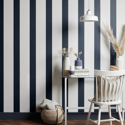 Blue and white vertical striped wallpaper with a glass table, white chair, ceramic vases, books, and a woven basket.