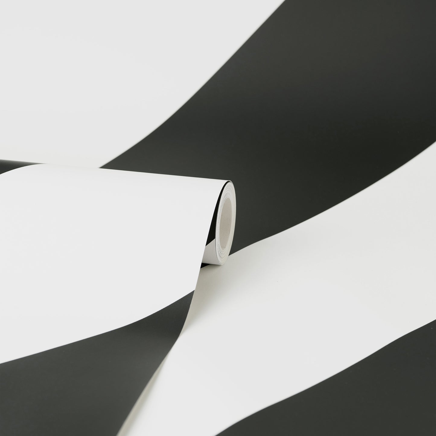 Close-up of a black & white striped wallpaper roll curling on a white surface with bold diagonal stripes.
