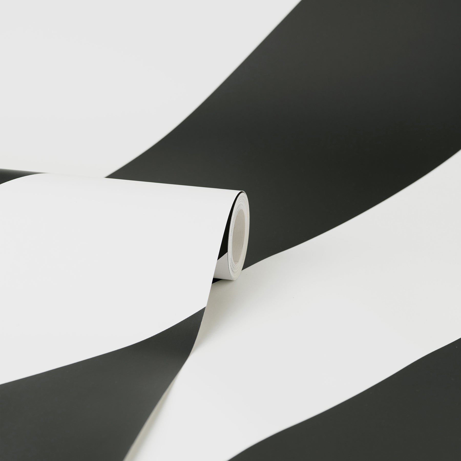 Close-up of a black & white striped wallpaper roll curling on a white surface with bold diagonal stripes.