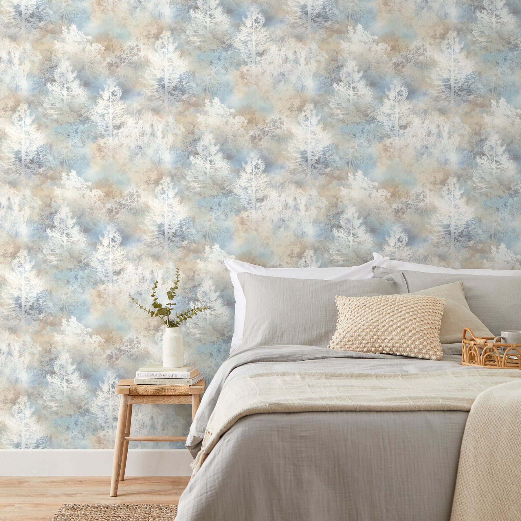 Cozy bedroom with gray bedding, beige pillow, light wood nightstand, vase of greenery, blue-beige tree-pattern wallpaper