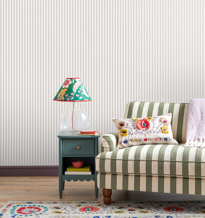 Teal painted end table with a clear glass base lamp & a bright floral shade beside a green-and-cream striped sofa; floral cushion & patterned rug.