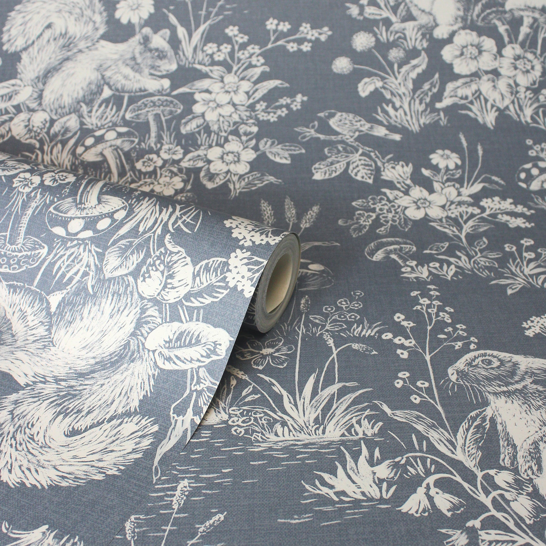 Blue-gray wallpaper featuring a white toile woodland scene with squirrels, birds & flowers; roll partially unrolled.