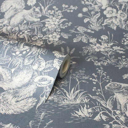 Blue-gray wallpaper featuring a white toile woodland scene with squirrels, birds & flowers; roll partially unrolled.