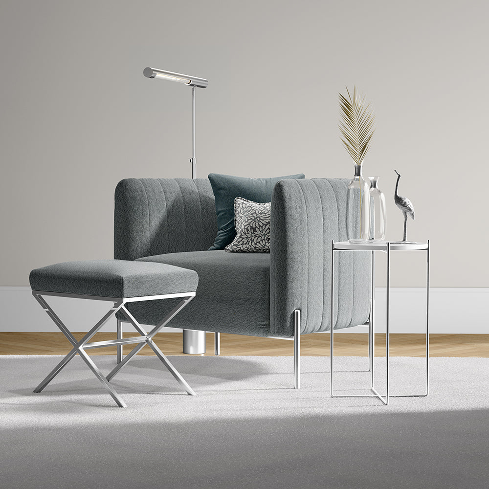 Grey channel-tufted sofa with matching ottoman on chrome legs, paired with glass-top side tables and modern floor lamp.