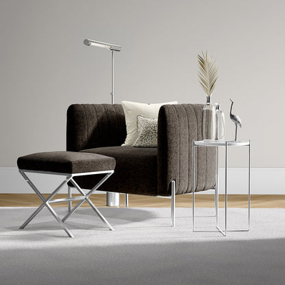 Dark brown modern sofa with chrome legs, matching ottoman, glass nesting tables, floor lamp, beige cushions and palm decor.