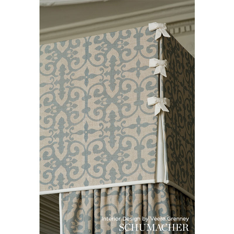 Damask patterned lilac and cream fabric-covered storage ottoman with white bow accents and a pleated skirt.