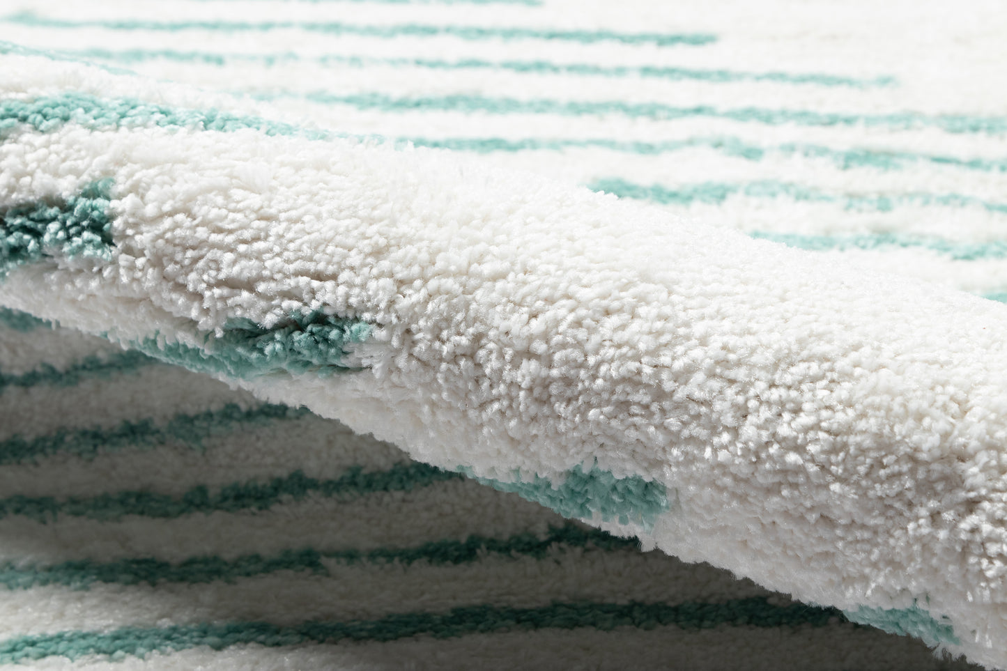 Close-up of white 2' x 3' rug with turquoise stripes, plush texture and rolled edge.