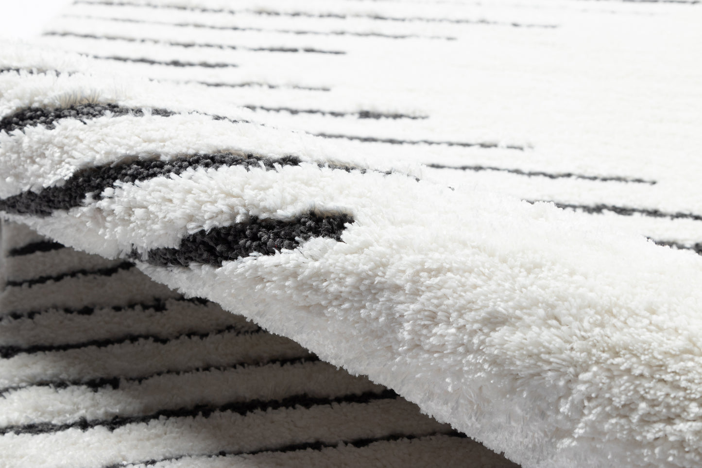 Soft white shag rug with black linear stripes and plush pile, folded edge.