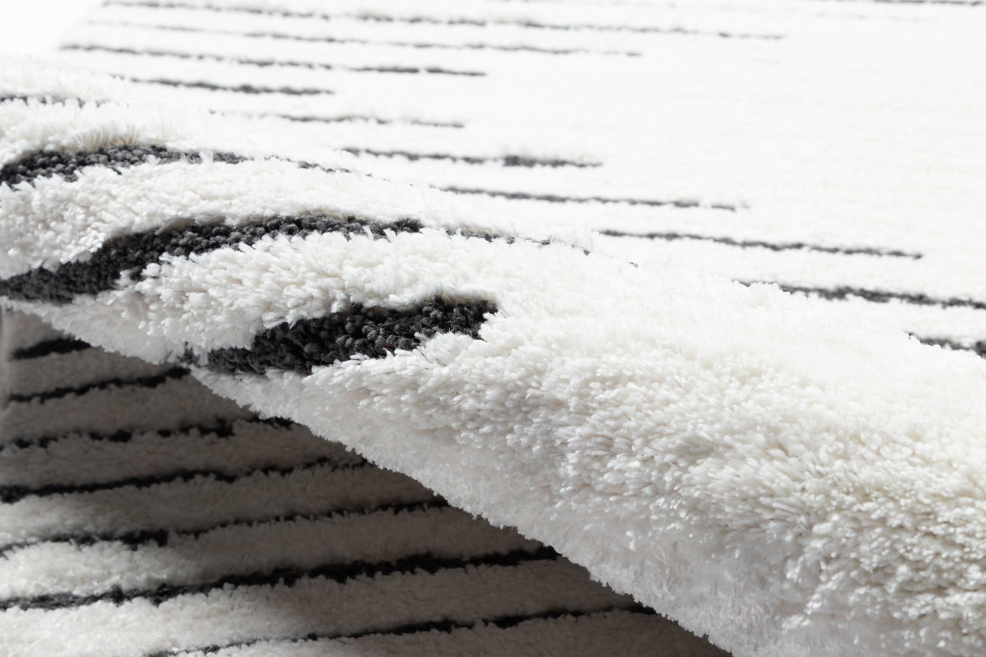 Soft white shag rug with black linear stripes and plush pile, folded edge.