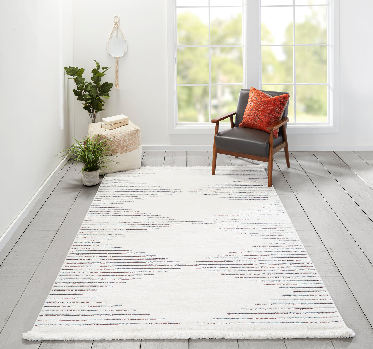 Ivory area rug with gray brushstroke pattern in a bright room with a wooden armchair and orange pillow.