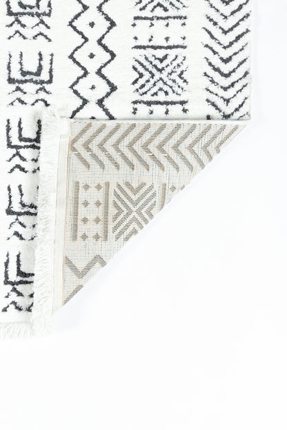 White textile rug with black geometric tribal print and fringe edges; folded to show beige chevron pattern on reverse.