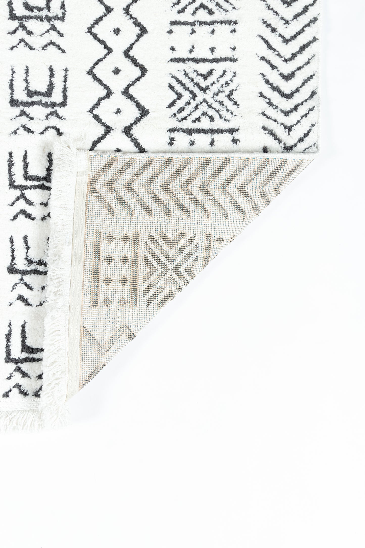 White rug with black tribal geometric patterns and fringe; folded corner reveals beige patterned underside.