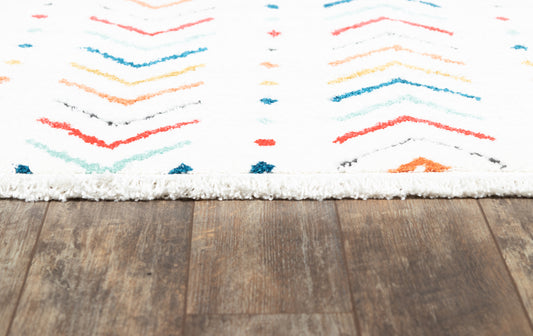 White fringed rug with colorful chevron stripes in red, orange, teal and blue on a wooden floor.