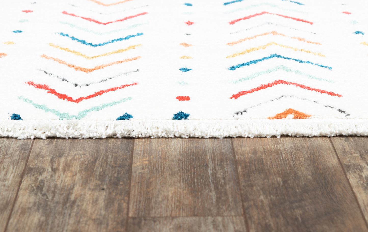 White shag rug with multicolor chevron pattern in red, blue, teal and orange on a wood floor.