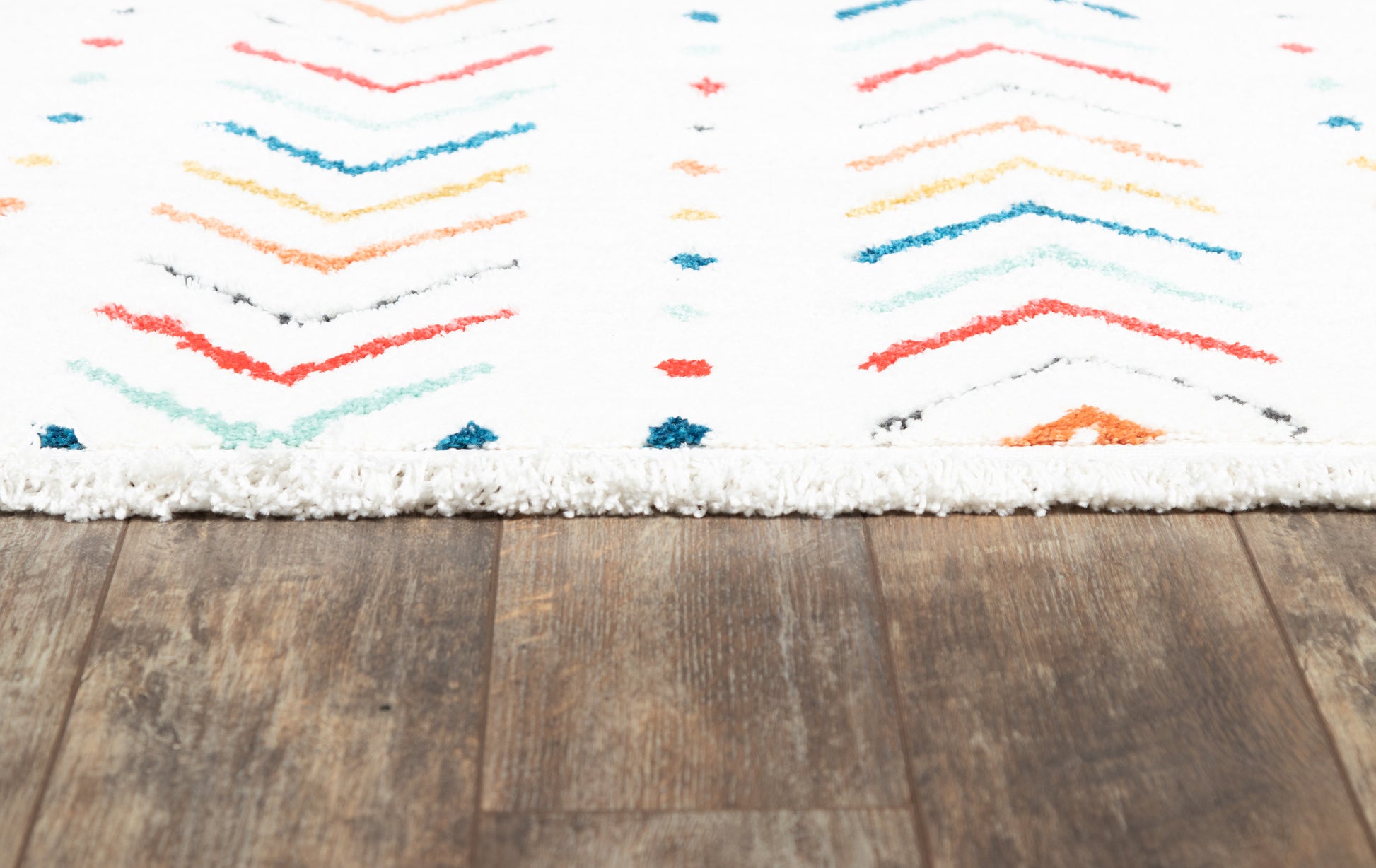 White shag rug with multicolor chevron pattern in red, blue, teal and orange on a wood floor.