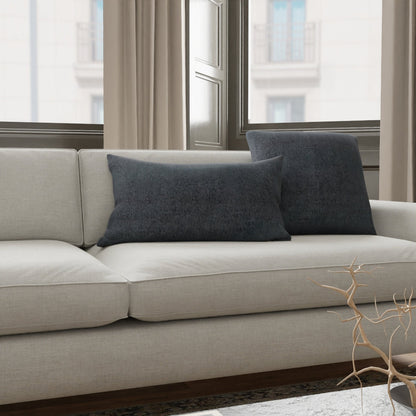 Beige fabric sofa with two dark blue cushions in a contemporary living room; light rug and bare branch decor by window.