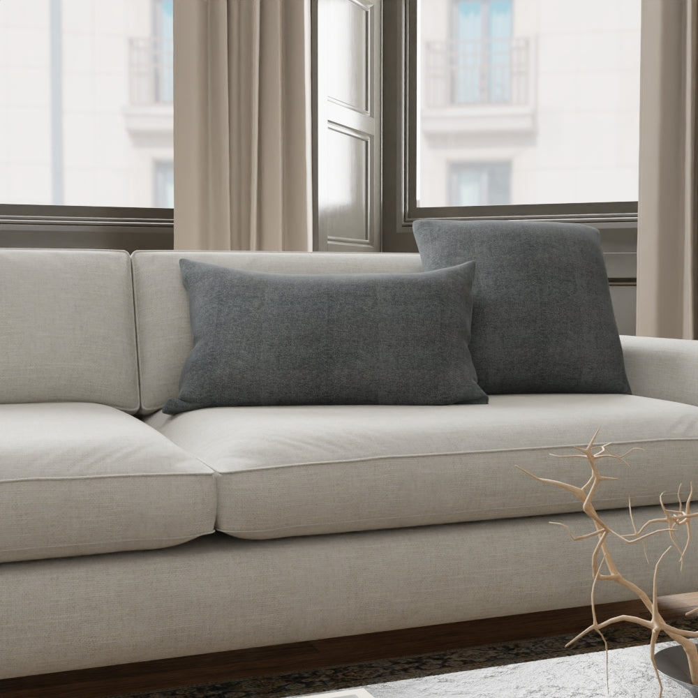 Beige fabric sofa with dark gray cushions in a modern living room by large windows.