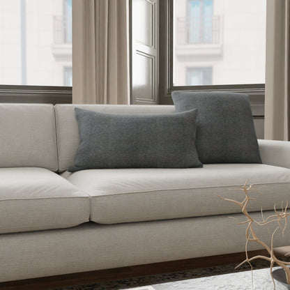 Beige fabric sofa with dark gray cushions in a modern living room by large windows.