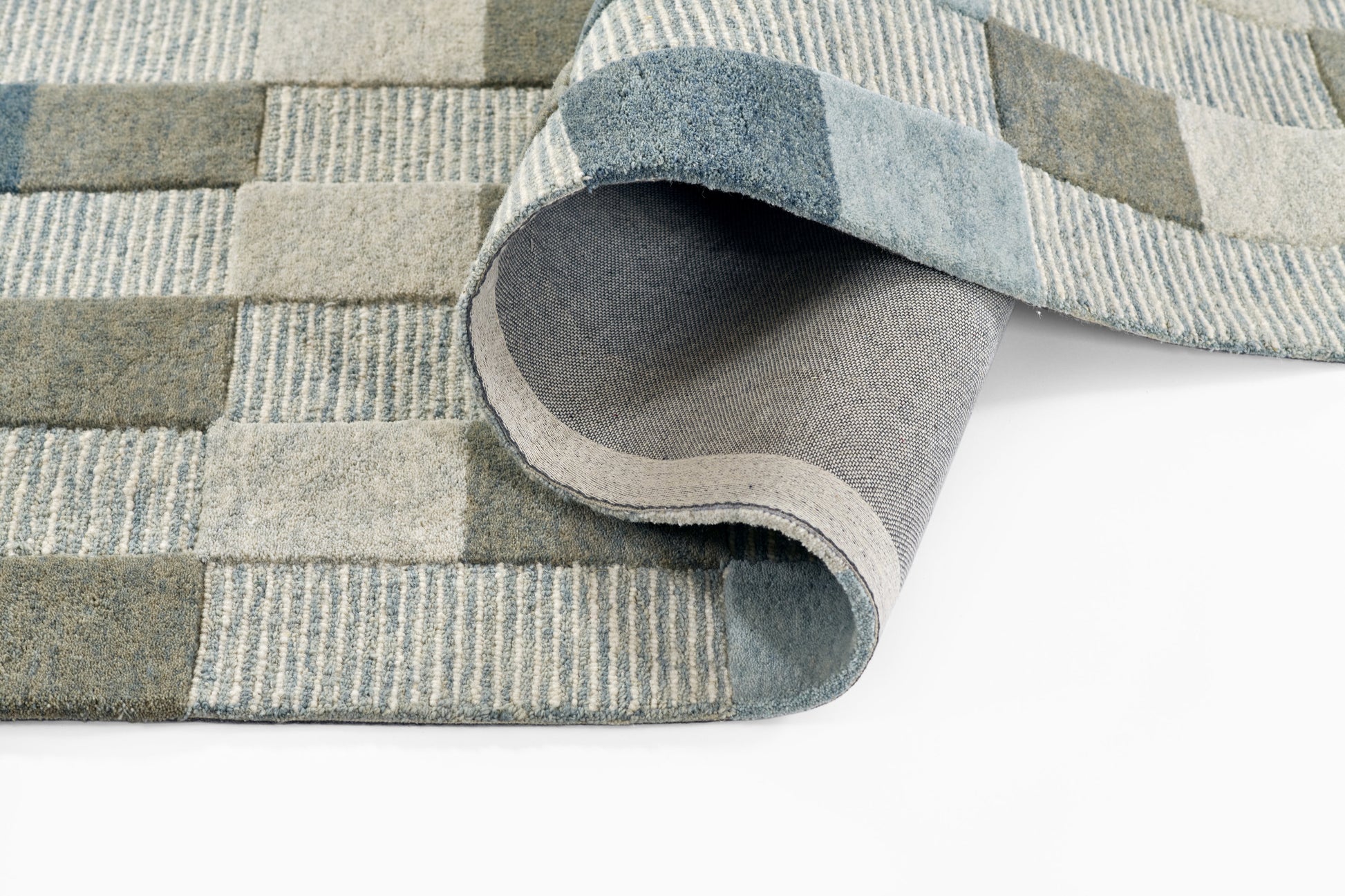 Blue-gray patchwork rug with woven stripe panels & rolled edge, soft modern floor decor.