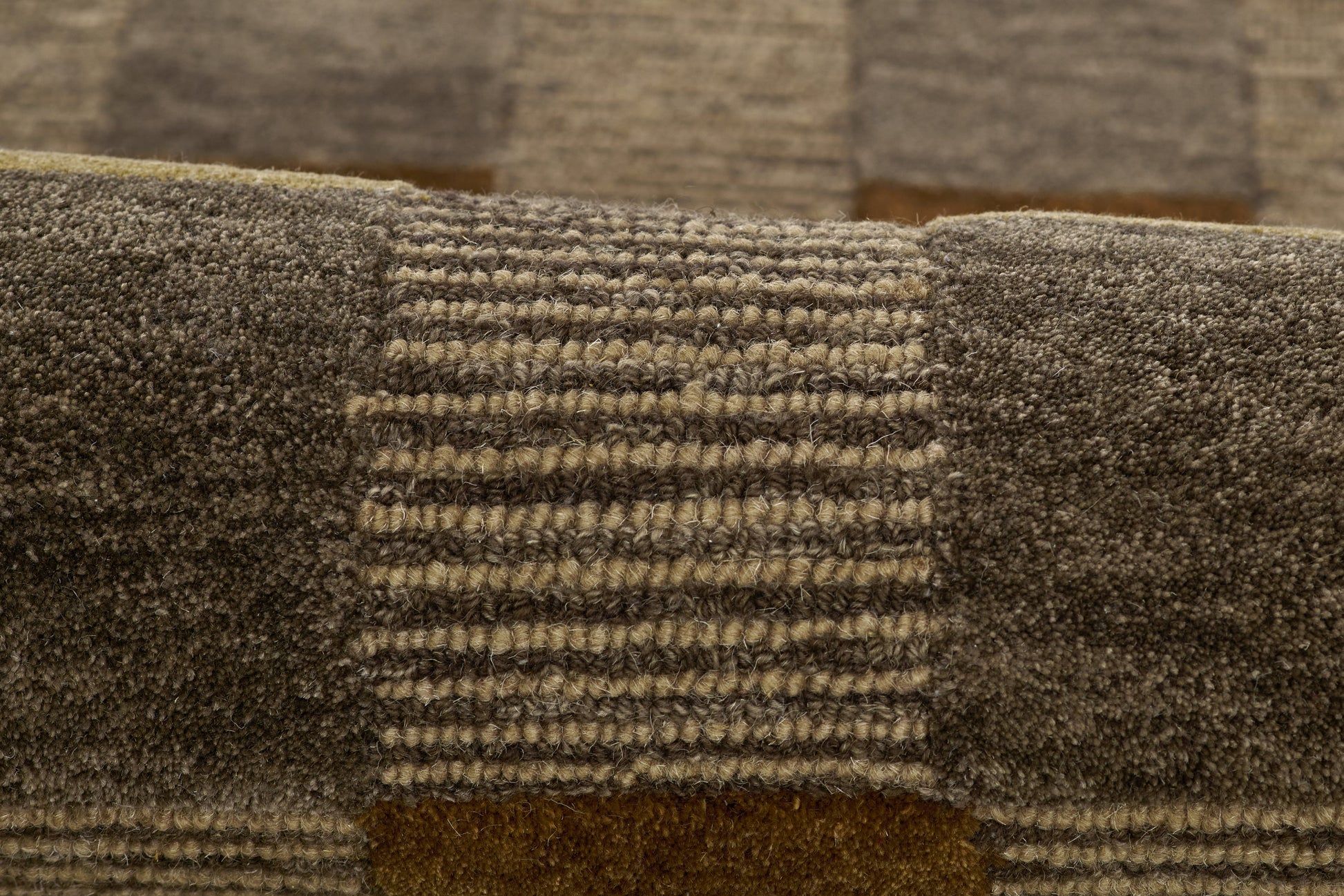 Close-up of brown patchwork rug with dark blocks and striped center panel, plush textured pile.