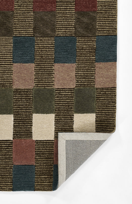 Geometric woven rug with a checkerboard of brown, tan, olive and slate blue; folded corner reveals grey backing.