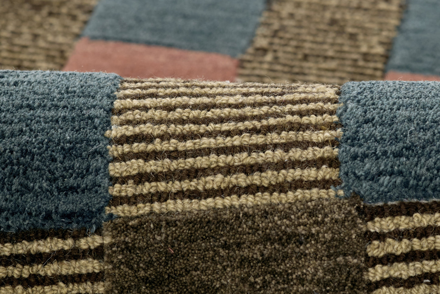 Close-up of a textured woven patchwork rug in blue, tan and brown blocks with striped sections.