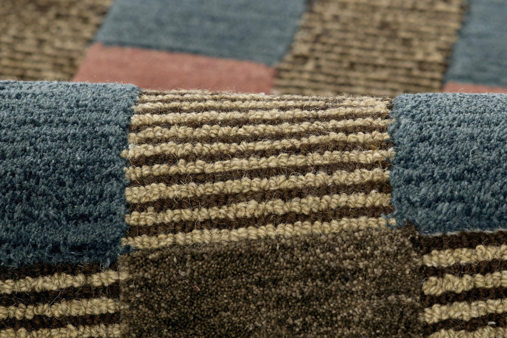 Close-up of a textured woven patchwork rug in blue, tan and brown blocks with striped sections.