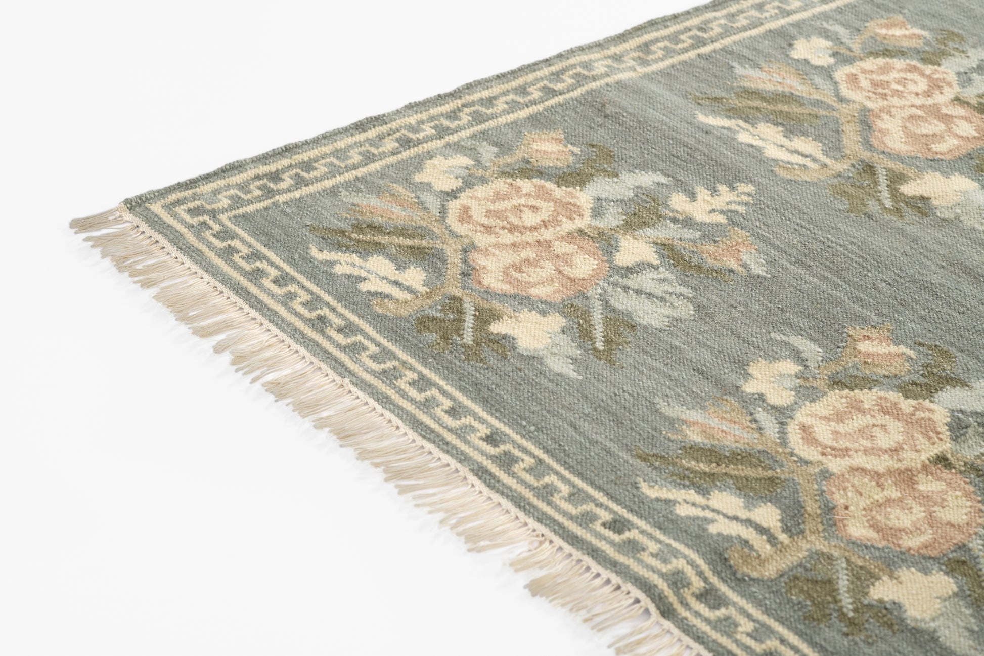 Blue-grey field rug with pink roses, sage leaves, fringe trim and Greek-key border.