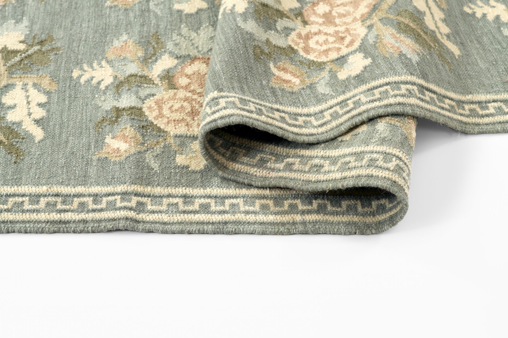 Floral blue-green area rug with beige flowers and Greek-key border; folded edge, vintage woven look.