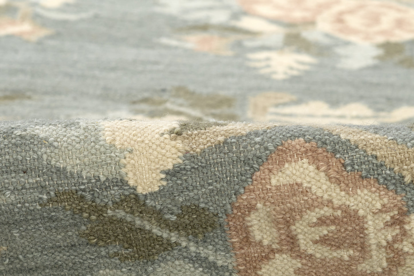 Close-up of a woven rug with blue-gray field and ivory floral damask pattern, beige-brown medallion accents