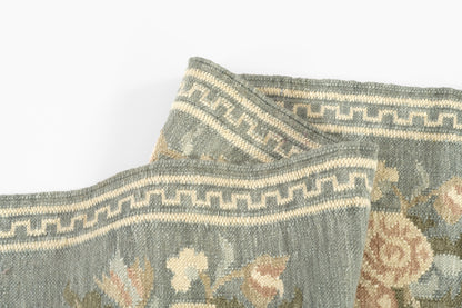 Blue-grey woven rug with beige floral pattern and Greek key border; soft tapestry texture.