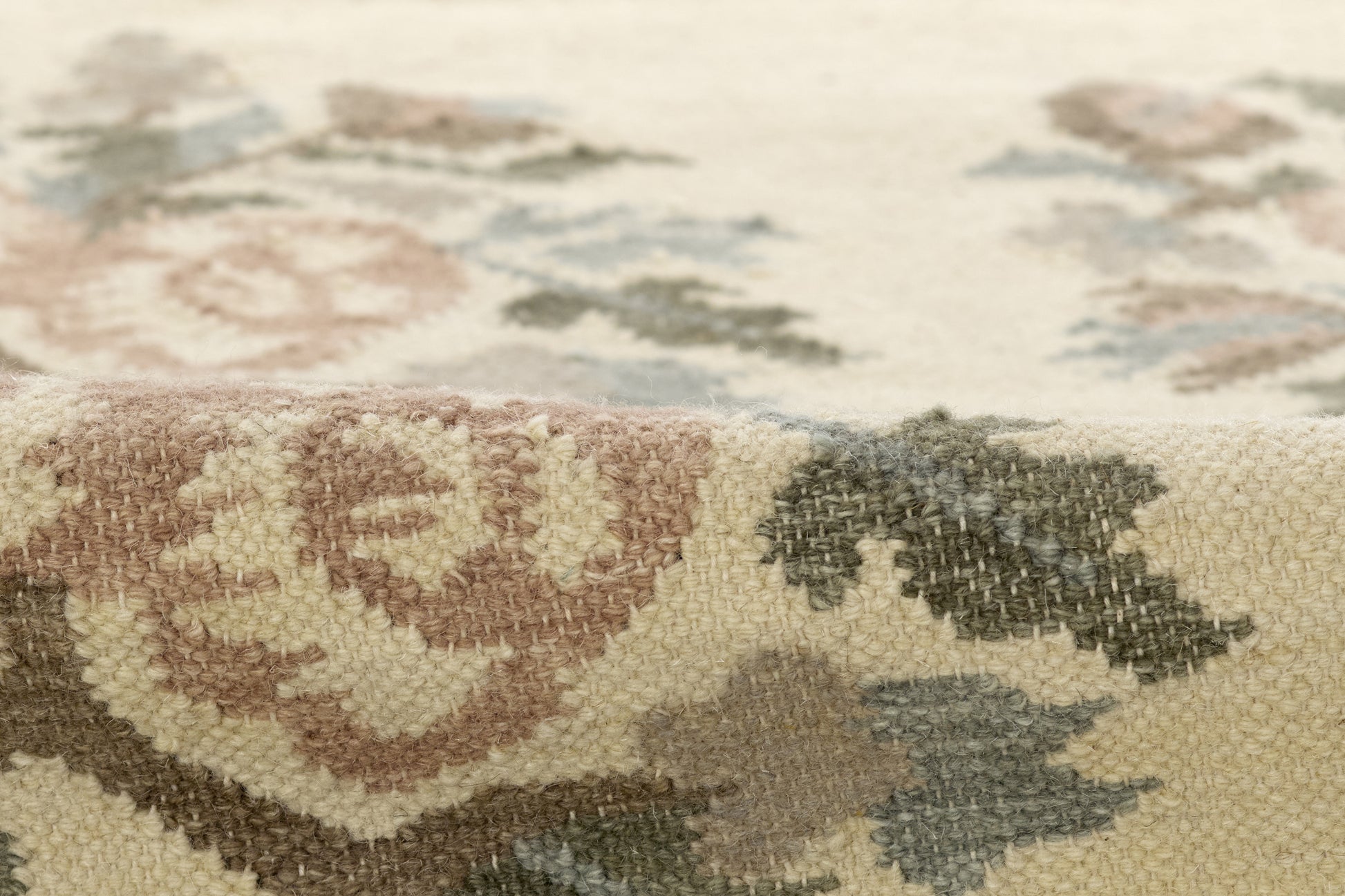 Close-up of a beige floral rug with ivory, brown, sage green and dusty blue motifs; woven textile.