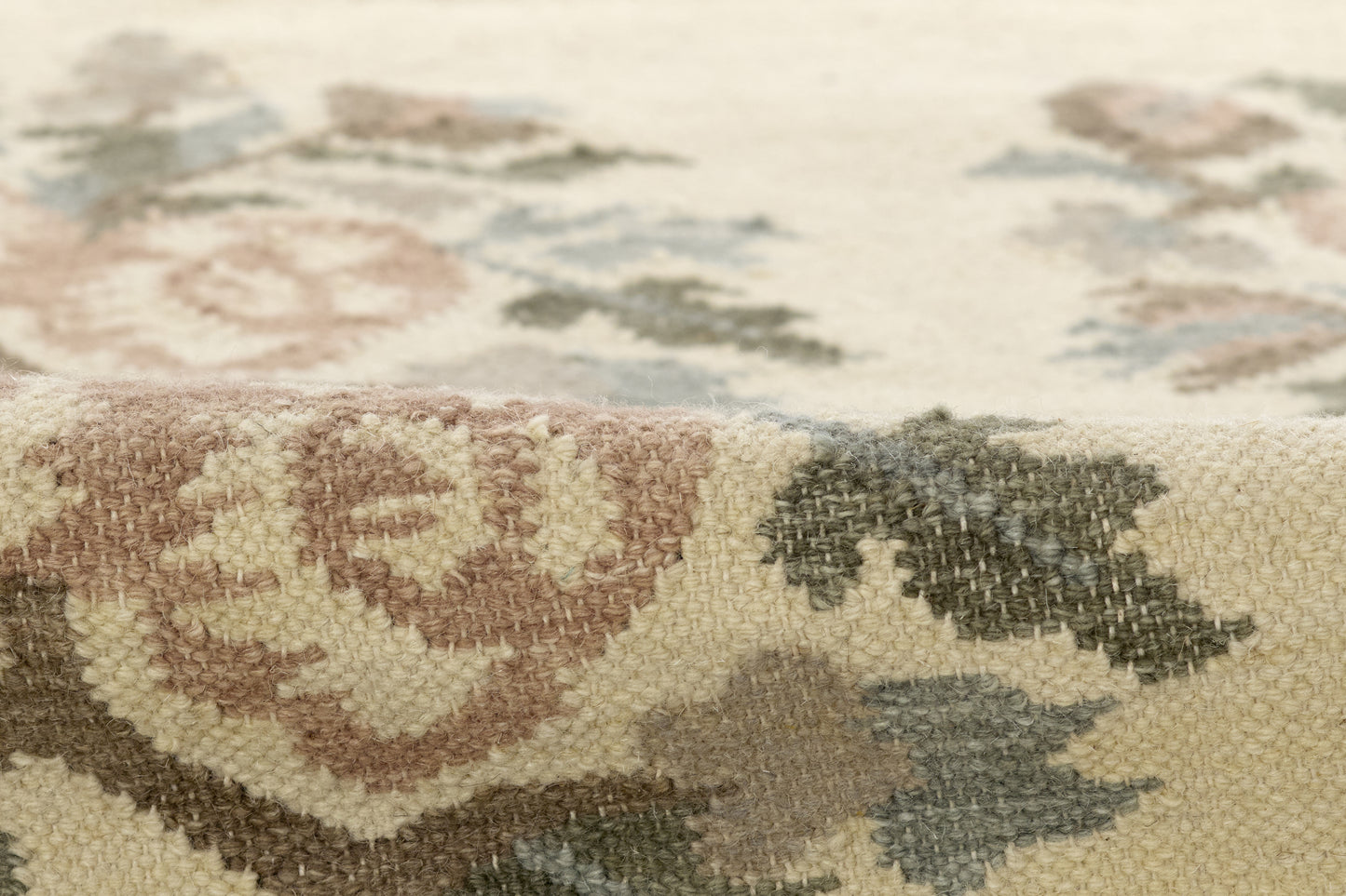 Close-up of a floral patterned rug with a beige woven base and pink, blue-gray, and sage-green leaves; neutral home decor.