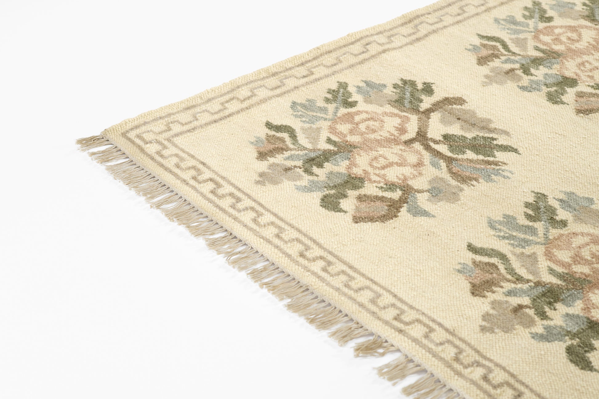 Beige floral rug with pink roses and green leaves, Greek-key border and fringe along edge.