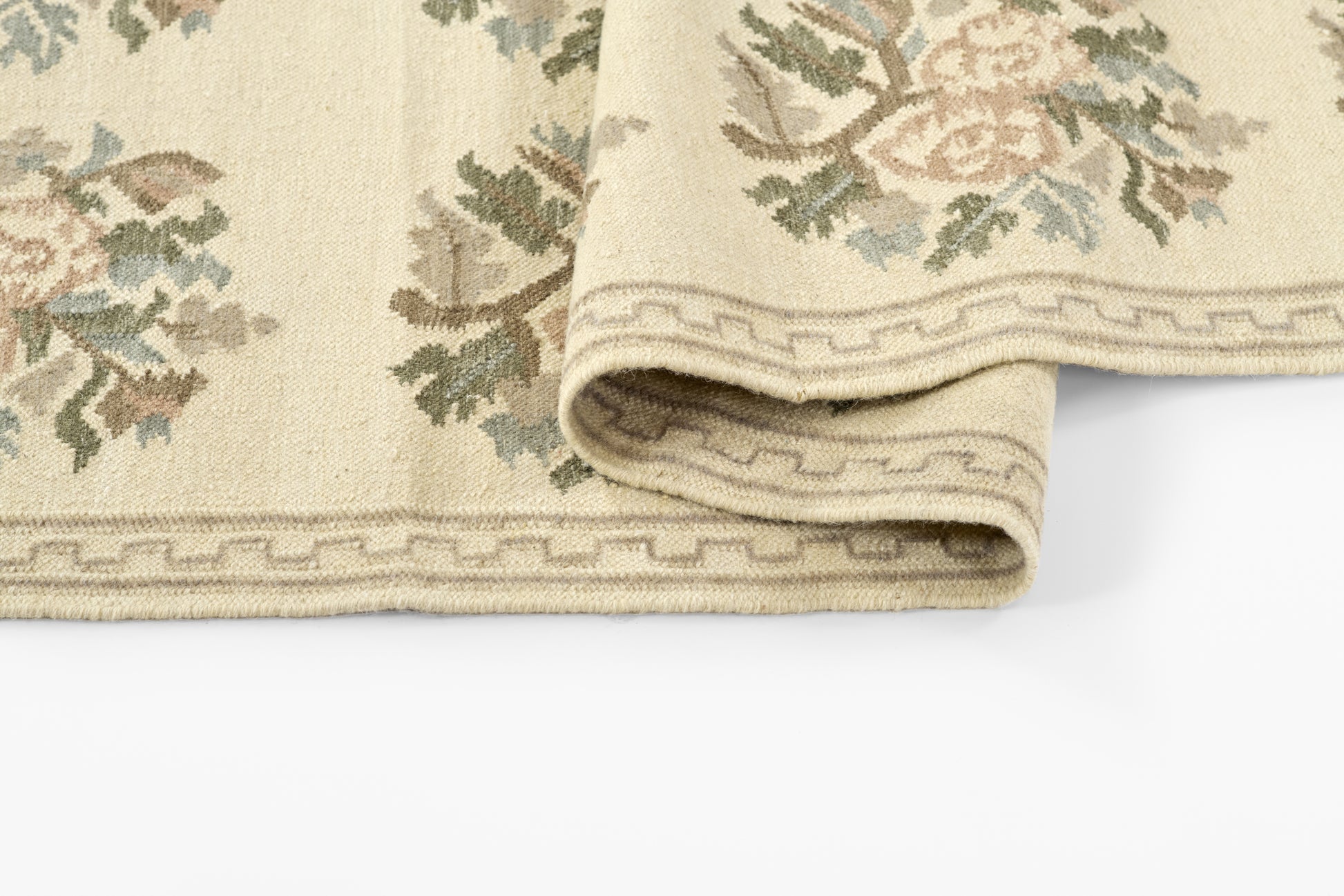 Beige floral woven area rug with pastel pink and green vines and Greek key border, folded edge.